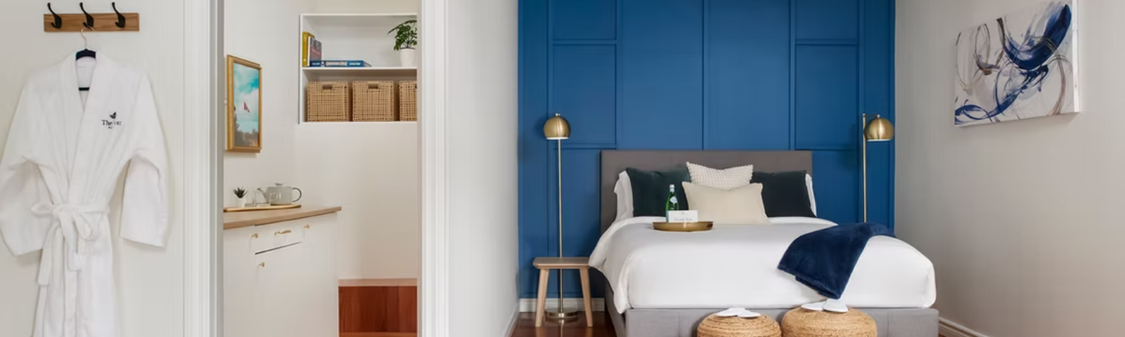 A hotel room with a bright blue headboard and a white robe hung by the closet door